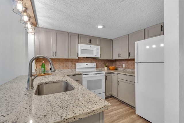 kitchen featuring sink, white appliances, light wood-type flooring, light stone countertops, and pendant lighting