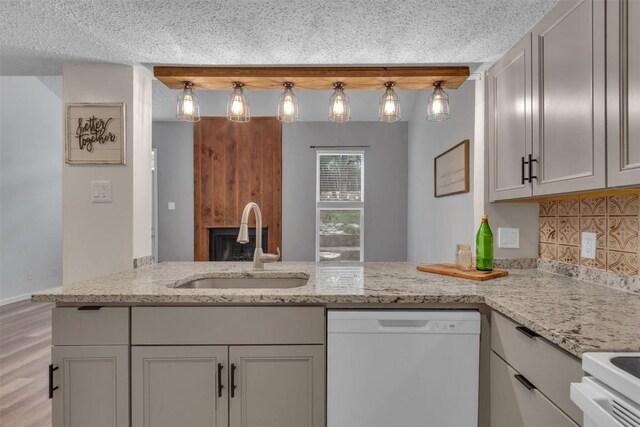 kitchen with kitchen peninsula, sink, hanging light fixtures, light stone counters, and white dishwasher