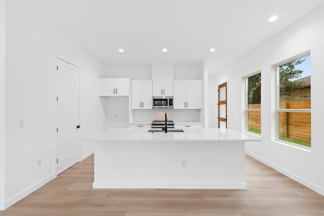 kitchen with a kitchen island with sink, white cabinetry, tasteful backsplash, sink, and light hardwood / wood-style floors