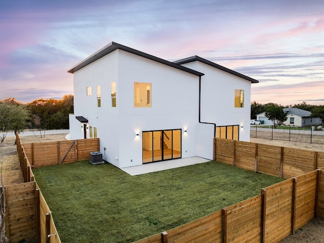 back house at dusk with central air condition unit, a yard, and a patio area