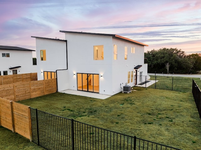 back house at dusk with central AC, a yard, and a patio area