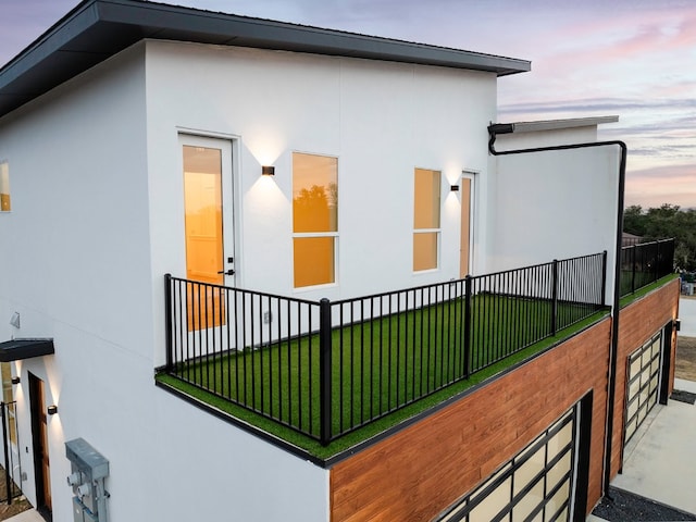 property exterior at dusk with a balcony and a yard