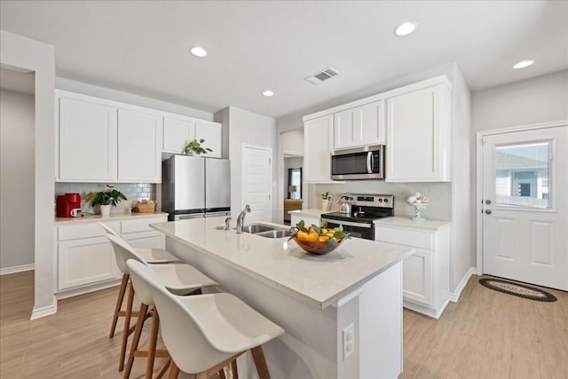 kitchen with light hardwood / wood-style flooring, appliances with stainless steel finishes, white cabinetry, a center island with sink, and a breakfast bar