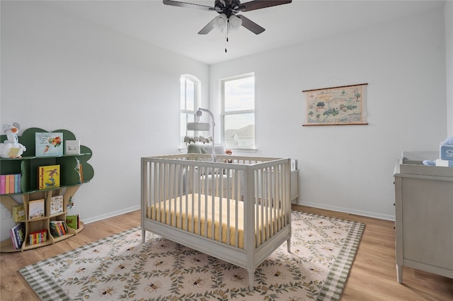 bedroom featuring a crib, light wood-type flooring, and ceiling fan