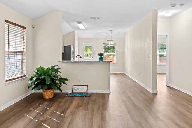 kitchen with pendant lighting, light wood-type flooring, light stone counters, kitchen peninsula, and stainless steel refrigerator