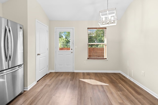 unfurnished dining area with wood-type flooring, lofted ceiling, and a notable chandelier