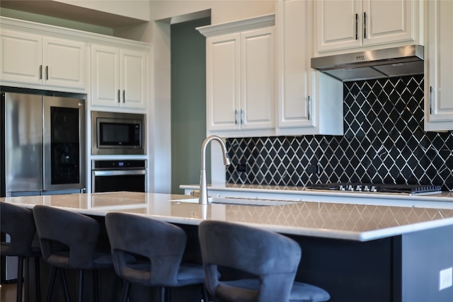 kitchen featuring ventilation hood, white cabinetry, stainless steel appliances, and a breakfast bar