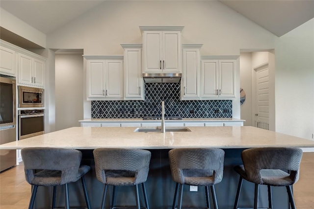 kitchen featuring a kitchen island with sink, stainless steel appliances, white cabinetry, backsplash, and under cabinet range hood