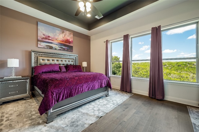 bedroom with ceiling fan, wood-type flooring, and a tray ceiling