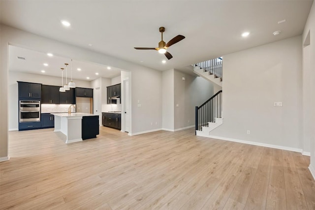 unfurnished living room with ceiling fan, sink, and light wood-type flooring