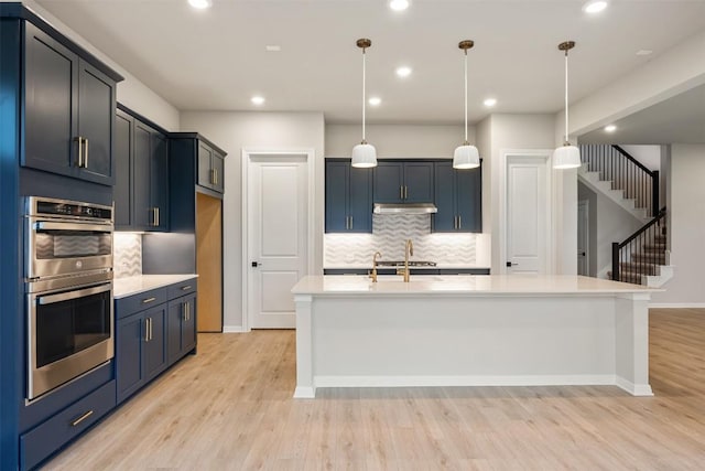 kitchen featuring decorative backsplash, stainless steel double oven, sink, decorative light fixtures, and an island with sink