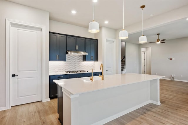 kitchen featuring backsplash, stainless steel gas stovetop, ceiling fan, hanging light fixtures, and an island with sink