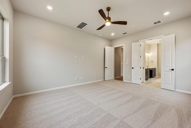 unfurnished bedroom featuring connected bathroom, light colored carpet, and ceiling fan