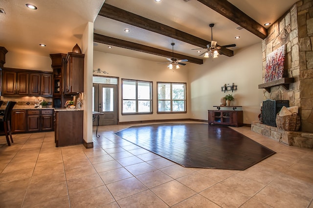 living room with ceiling fan, light tile patterned floors, beam ceiling, and a stone fireplace