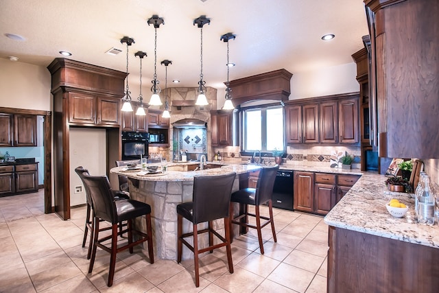 kitchen featuring pendant lighting, light stone countertops, black appliances, and a kitchen island with sink