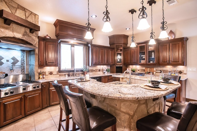 kitchen featuring stainless steel gas cooktop, a breakfast bar area, an island with sink, and hanging light fixtures