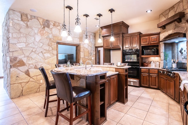 kitchen with decorative light fixtures, light stone countertops, black appliances, a kitchen island with sink, and a breakfast bar