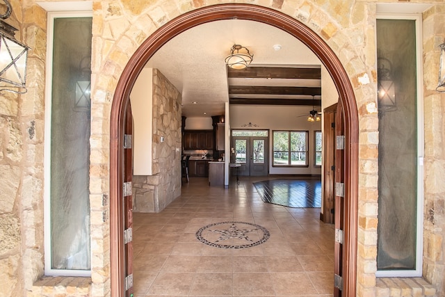 hallway featuring a textured ceiling, beamed ceiling, and light tile patterned floors