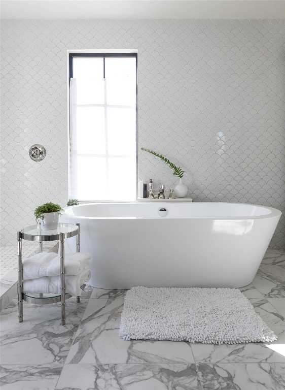 bathroom with a tub to relax in, plenty of natural light, and tile walls