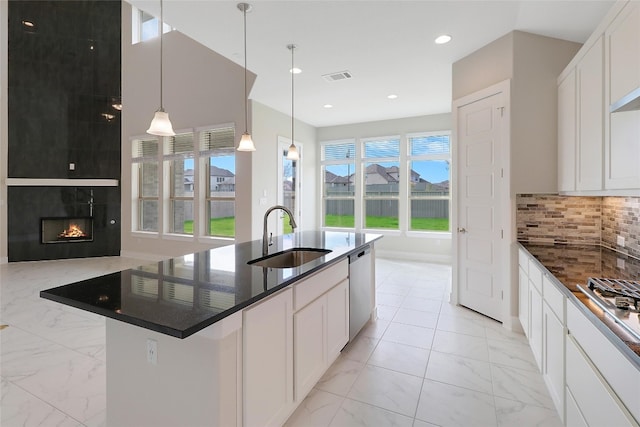 kitchen featuring a tile fireplace, an island with sink, white cabinetry, and sink