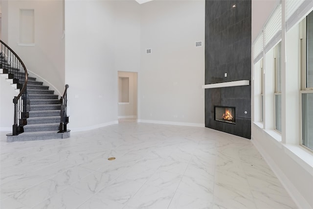 unfurnished living room featuring a tiled fireplace and a high ceiling