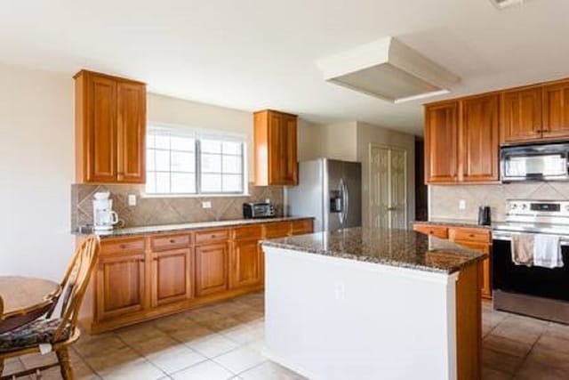 kitchen featuring a kitchen island, stainless steel appliances, dark stone counters, and tasteful backsplash