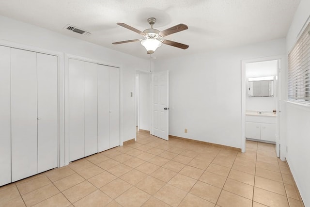 unfurnished bedroom with ceiling fan, light tile patterned floors, ensuite bathroom, and multiple closets