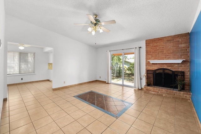 unfurnished living room with ceiling fan, light tile patterned floors, a textured ceiling, and a brick fireplace