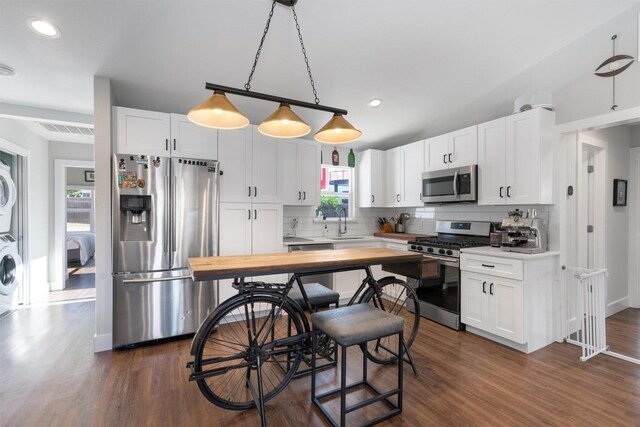 kitchen with white cabinetry, stainless steel appliances, decorative light fixtures, stacked washing maching and dryer, and dark hardwood / wood-style floors