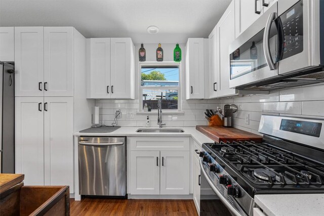 kitchen with tasteful backsplash, appliances with stainless steel finishes, white cabinetry, wood-type flooring, and sink