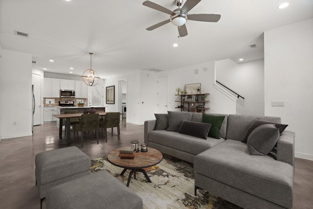 living room featuring ceiling fan with notable chandelier and concrete flooring