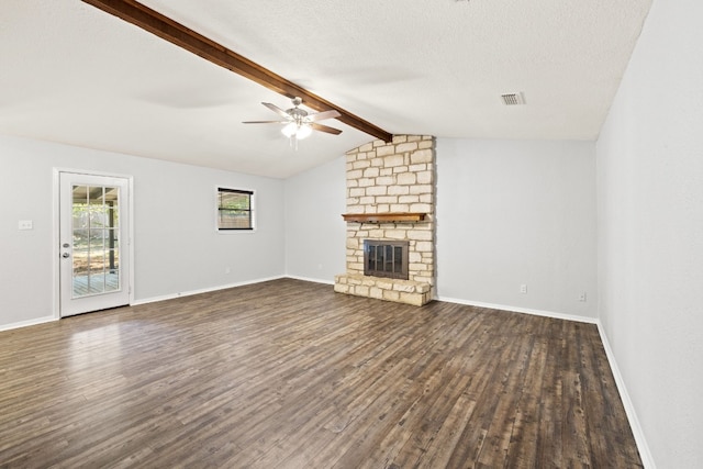 unfurnished living room featuring a textured ceiling, dark hardwood / wood-style flooring, a stone fireplace, lofted ceiling with beams, and ceiling fan