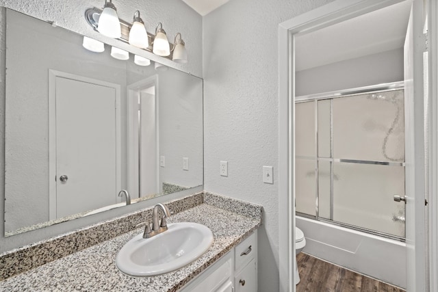 full bathroom featuring wood-type flooring, toilet, combined bath / shower with glass door, and vanity