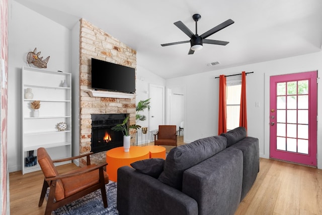 living room with light wood-type flooring, lofted ceiling, ceiling fan, and a stone fireplace