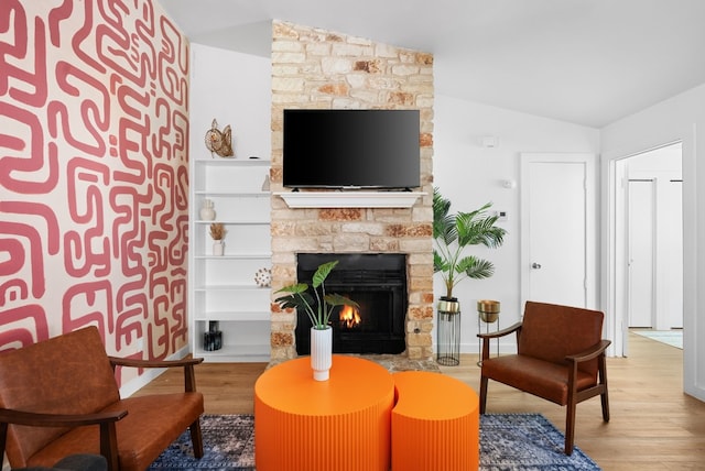 living room featuring vaulted ceiling, a stone fireplace, and wood-type flooring