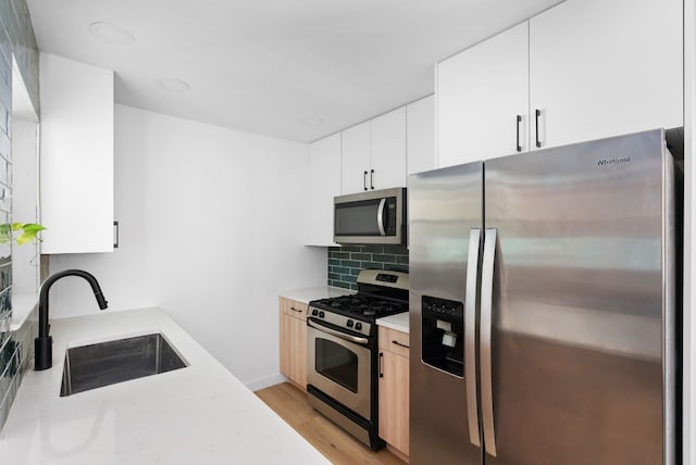 kitchen featuring backsplash, light hardwood / wood-style flooring, stainless steel appliances, white cabinetry, and sink