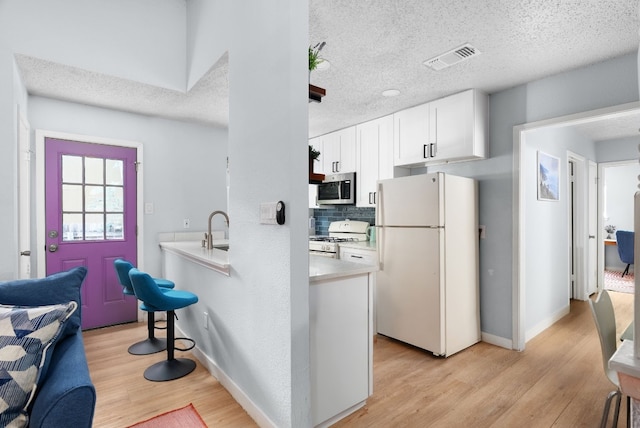 kitchen with a textured ceiling, white appliances, white cabinetry, and light hardwood / wood-style floors