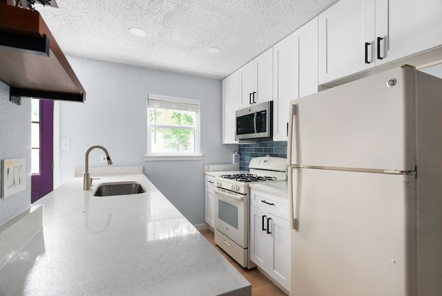 kitchen with white cabinetry, white appliances, a textured ceiling, light stone counters, and sink