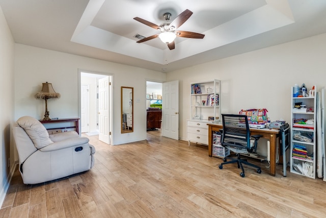 home office with a raised ceiling, ceiling fan, and light wood-type flooring