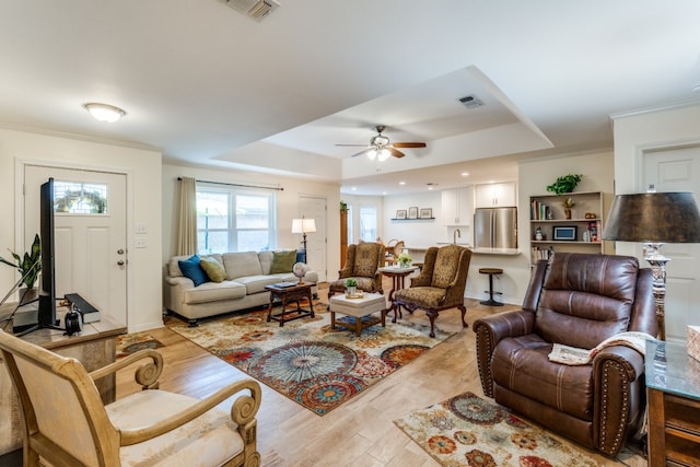 living room with a tray ceiling, ceiling fan, light hardwood / wood-style floors, and ornamental molding