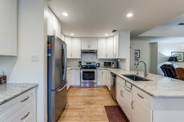 kitchen with stainless steel appliances, kitchen peninsula, sink, white cabinets, and light hardwood / wood-style floors