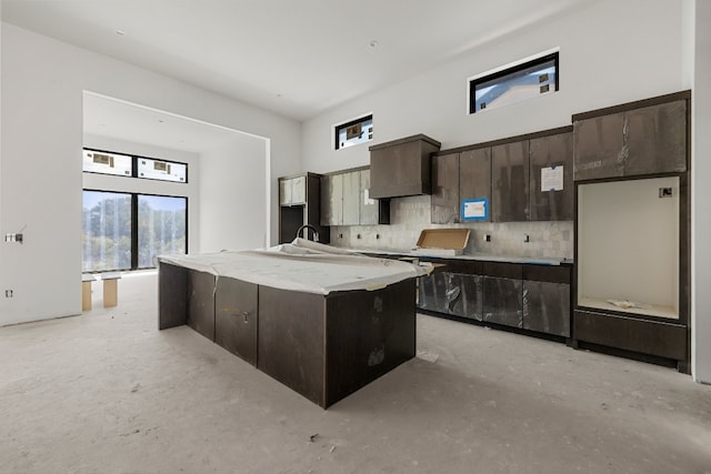 kitchen featuring tasteful backsplash, a kitchen island with sink, sink, a towering ceiling, and dark brown cabinetry