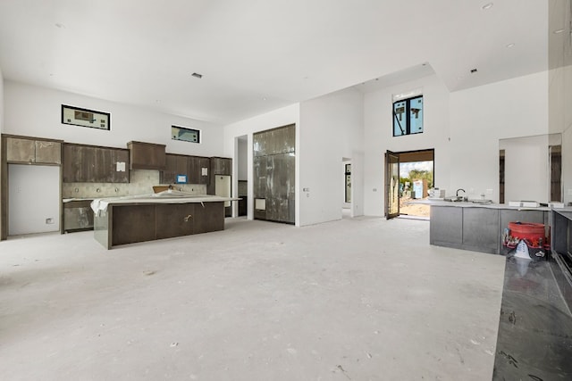 kitchen featuring a center island, a high ceiling, dark brown cabinetry, and backsplash