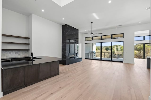 kitchen with sink, a large fireplace, a high ceiling, light hardwood / wood-style floors, and dark brown cabinets