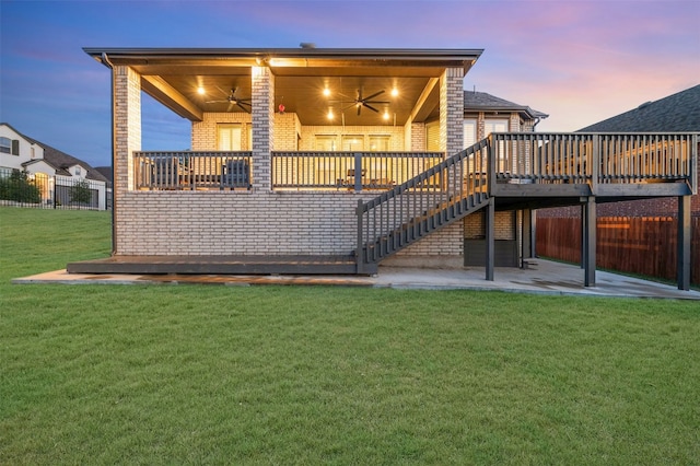 back house at dusk with a wooden deck, a yard, and ceiling fan