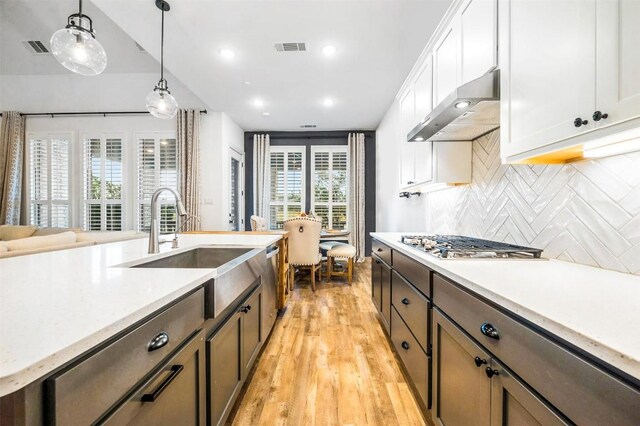 kitchen with sink, stainless steel appliances, white cabinets, decorative backsplash, and decorative light fixtures