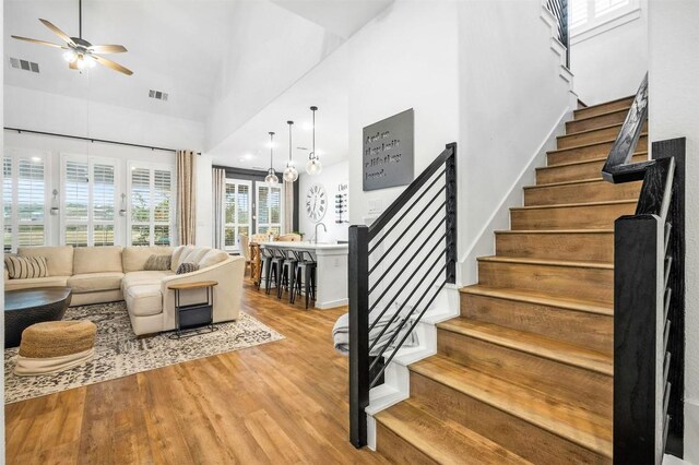 living room featuring sink, a towering ceiling, ceiling fan, and light wood-type flooring