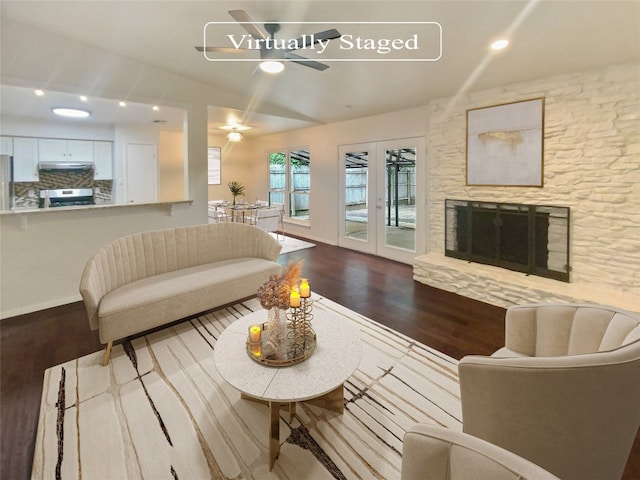 living room featuring hardwood / wood-style flooring, ceiling fan, and a stone fireplace