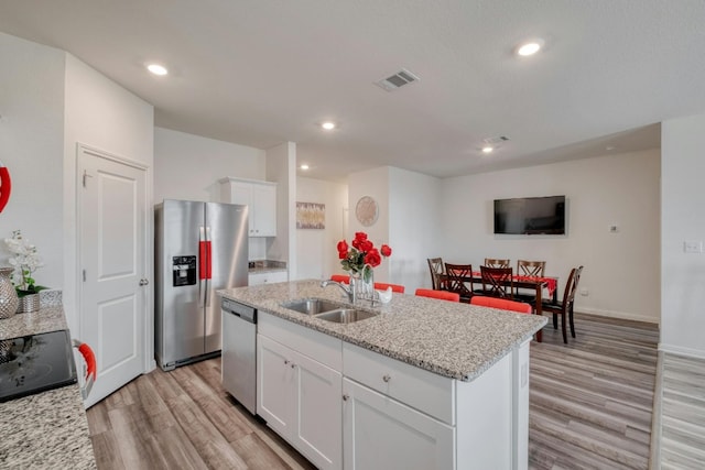 14601 Shooter Mc Gavin Dr, Manor, TX 78653 - kitchen with appliances with stainless steel finishes, light wood-style flooring, white cabinets, a kitchen island with sink, and light stone countertops