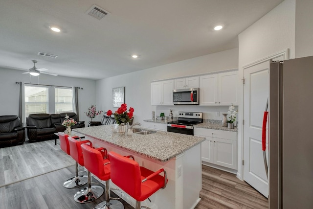 kitchen featuring a kitchen breakfast bar, light hardwood / wood-style flooring, appliances with stainless steel finishes, a kitchen island with sink, and white cabinetry